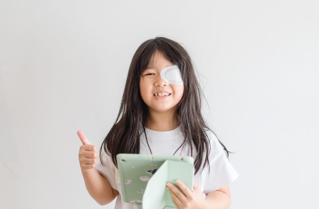 Young smiling girl holding a green iPad wears an occlusion patch on her left eye.