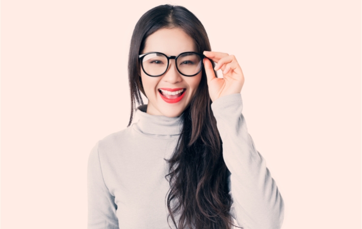Young smiling woman with black glasses standing in front of a lightly colored background.