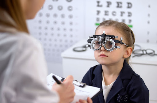 A young girl is optical trial frame while the ophthalmologist is writing down a prescription.