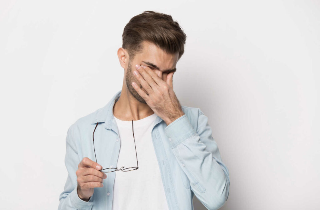 A man standing taking off his eyeglasses rubbing his eyes with his fingers due to eye problems.