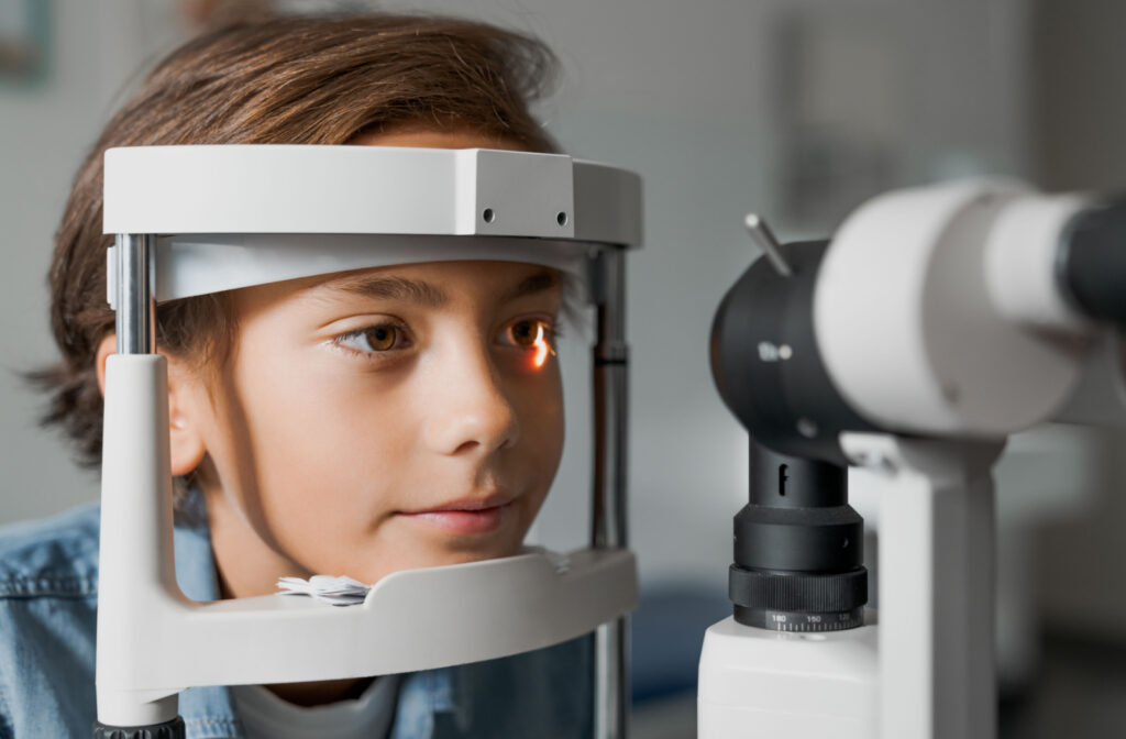 A boy sitting in an optometrist's office looking into a machine that tests his vision.