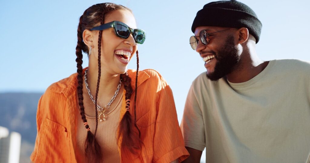 a female and male wearing sunglasses outside and are smiling.