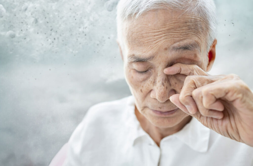 An older adult patient rubs their eye in an attempt to clear the double vision caused by a cataract.