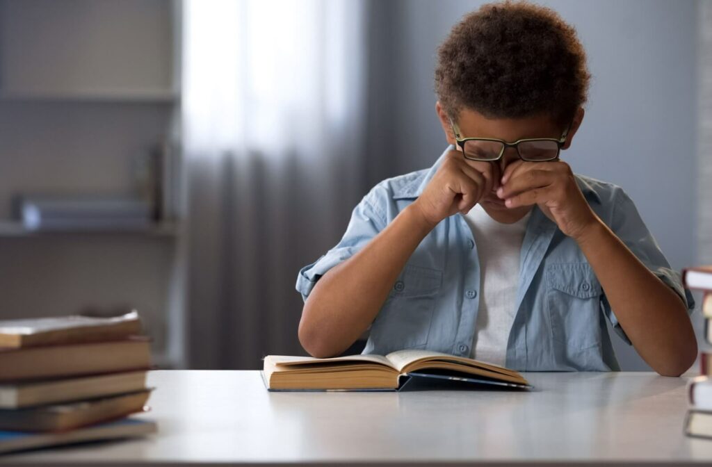 A child rubs his tired eyes while reading a book.