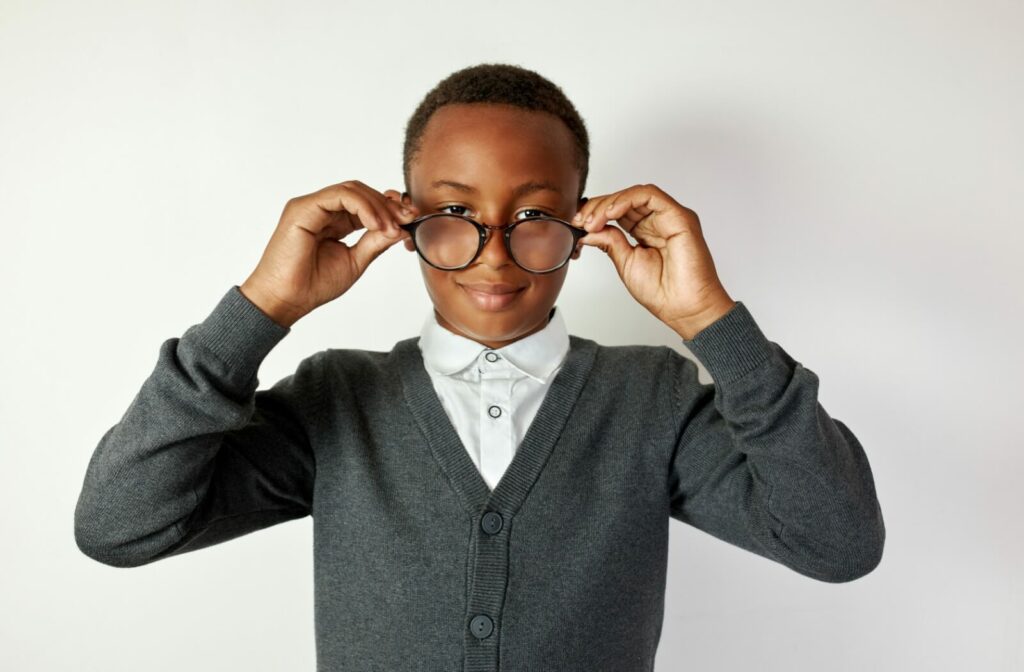 A preteen in a grey cardigan holds matching glasses to his face.