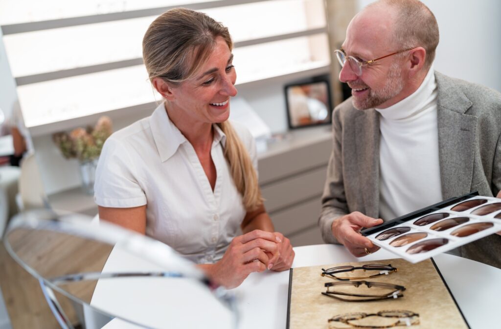 A patient and an optician smiling while reviewing prescription lens options for sunglasses at a table.