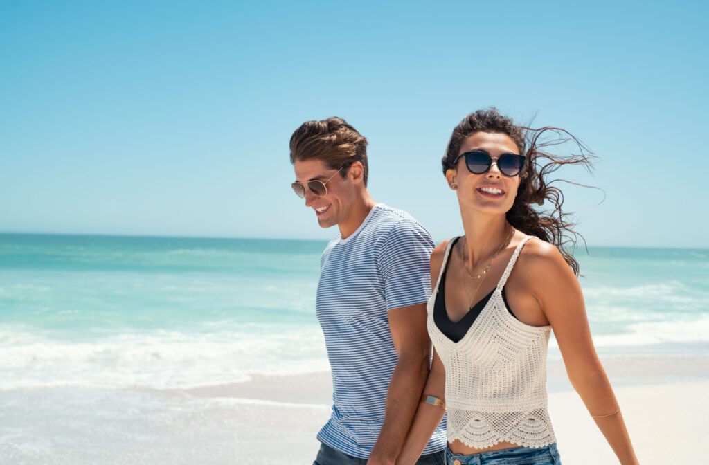 A smiling couple wearing polarized sunglasses enjoy a beach walk on a sunny day.